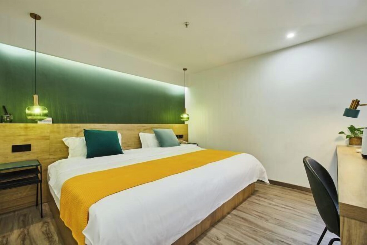 A modern hotel room with a large bed, wooden headboard, and a desk with a chair.