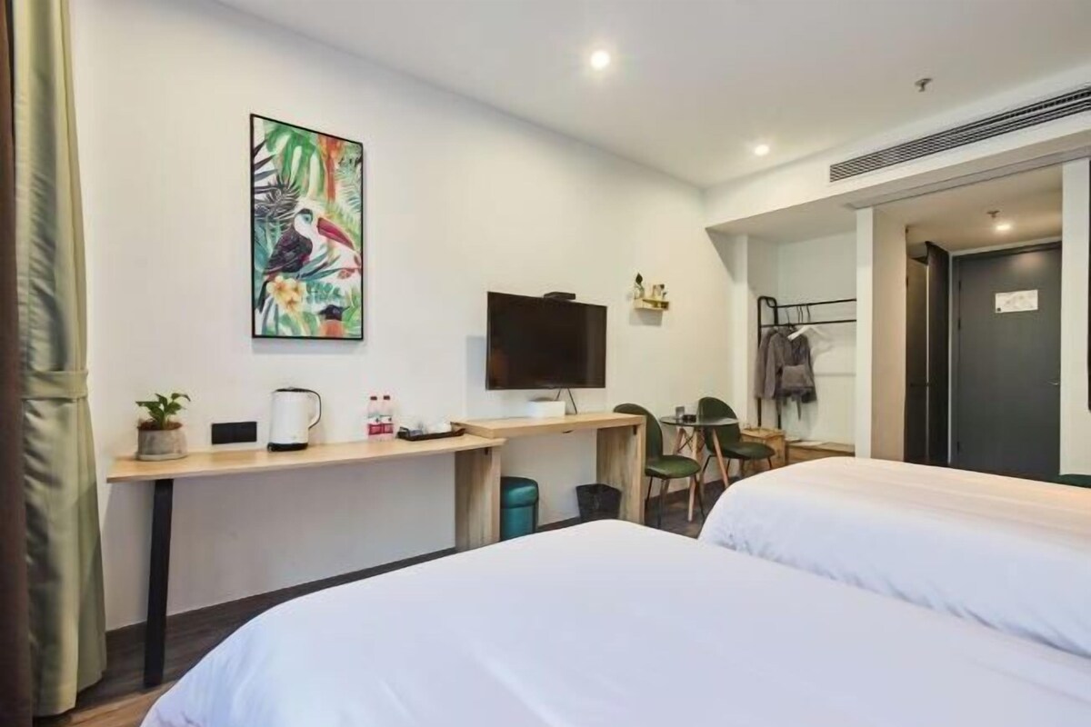 A hotel room with two beds, a desk with a TV, a small table, a chair, and a coat rack.