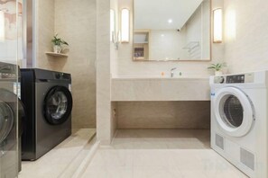 A compact hotel bathroom with a washing machine, a sink, and a mirror. - Vienna International Hotel (Wuxuan Chengbei Road) (Wuxuan)