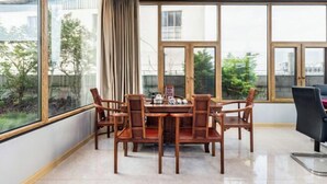 Een eetruimte met een houten tafel en stoelen, grote ramen en uitzicht op groen.