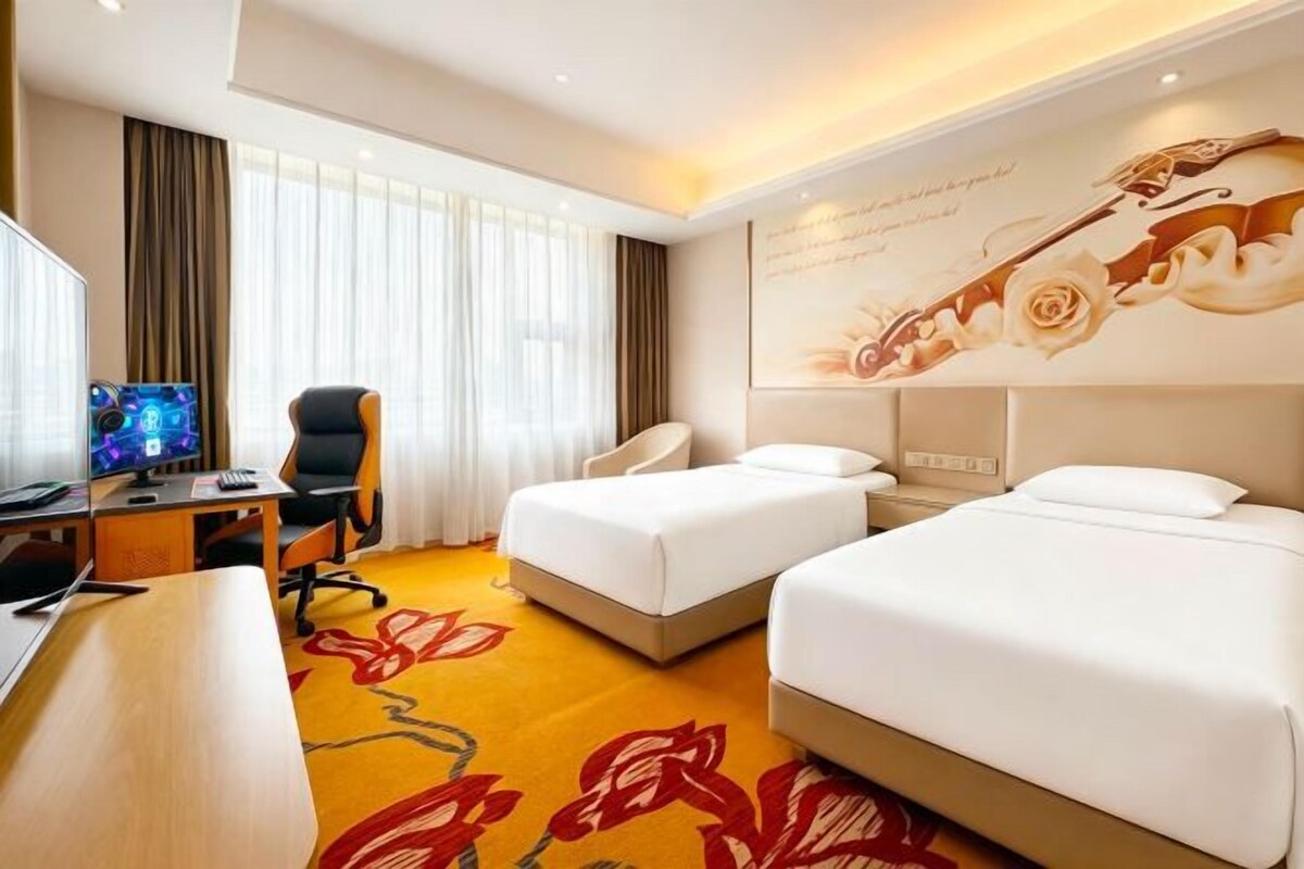 A hotel room with two beds, a desk with a computer, a chair, and a large window with curtains.