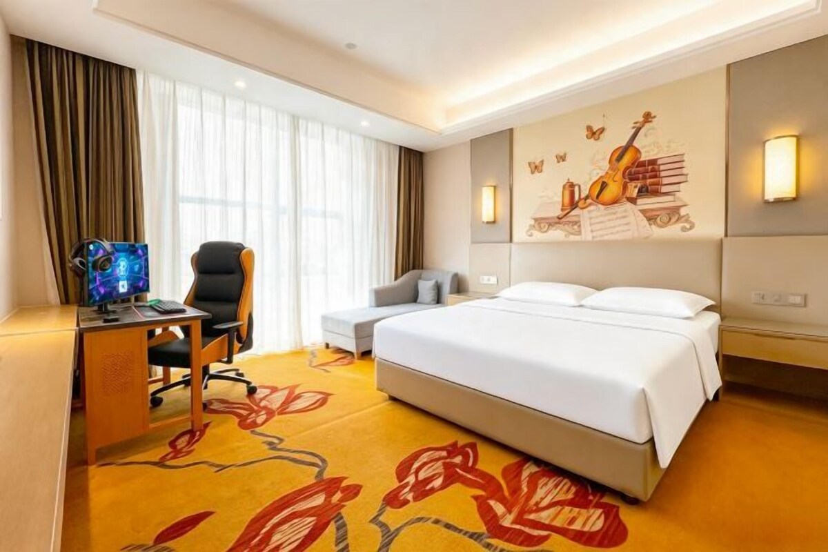 A hotel room with a bed, desk, chair, and a large window.