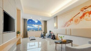 Een moderne hotelkamer met een grote televisie, fitnessapparatuur, een klein tafeltje en uitzicht op de lucht door een groot raam.
