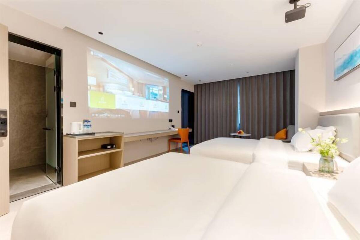 Ein Hotelzimmer mit zwei Betten, einem Schreibtisch, einem Stuhl, einem Fernseher und einem großen Fenster mit Vorhängen.