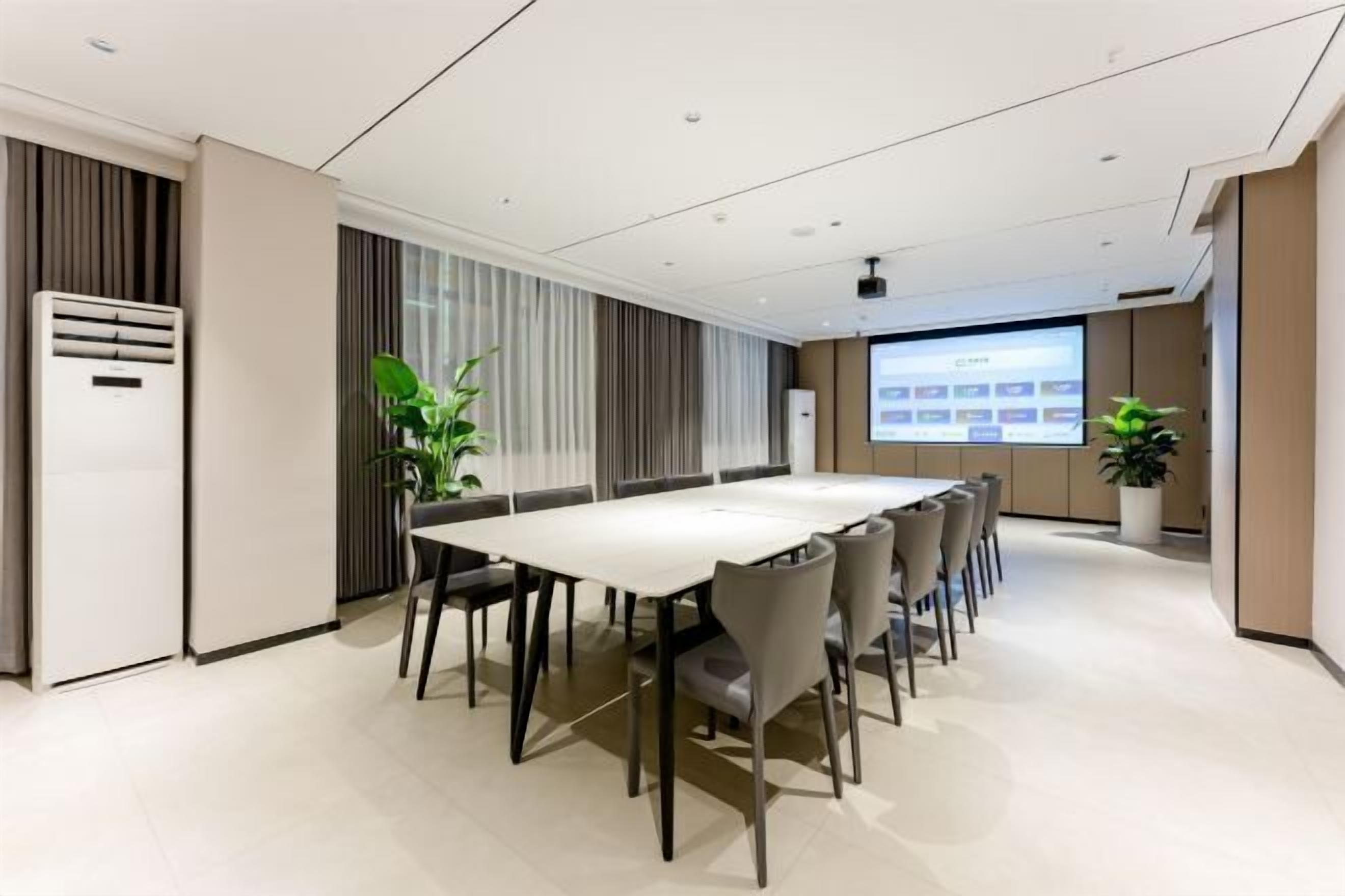 Een moderne vergaderzaal met een lange tafel, stoelen, een projectiescherm en potplanten.