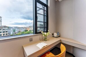 Une pièce d’angle avec une fenêtre, un bureau, une chaise et un vase rempli de fleurs.
