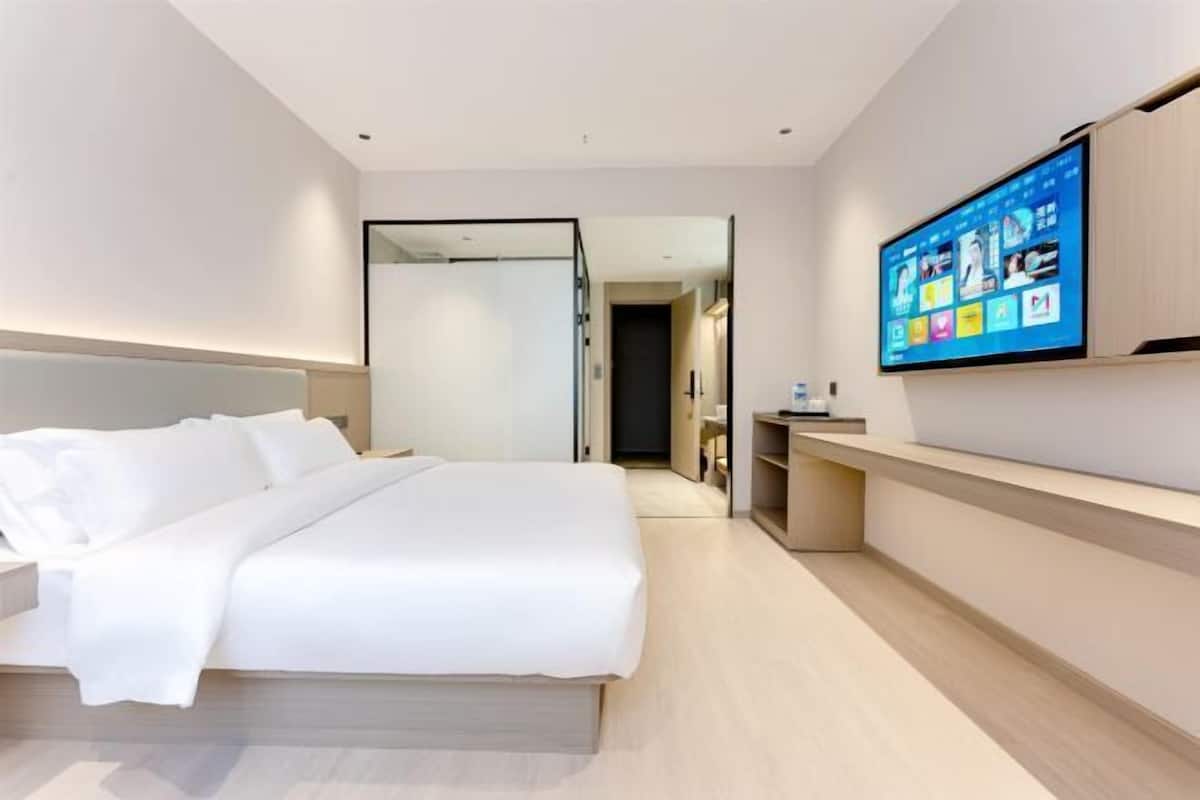 Ein modernes Hotelzimmer mit einem großen Bett, einem flachbildfernseher an der Wand und einem begehbaren Kleiderschrank.