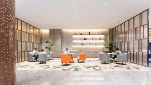 Eine moderne Lobby mit Marmorboden, Sitzbereichen mit grau und orangefarbenen Stühlen und einer Wand mit Regalen, die verschiedene Gegenstände zeigen.