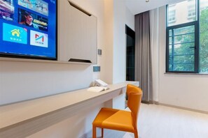 Un espace d’accueil d’hôtel avec un téléviseur à écran plat fixé au mur, affichant différentes icônes d’applications, un comptoir de réception avec un téléphone et un livre, et une fenêtre donnant sur un paysage verdoyant.