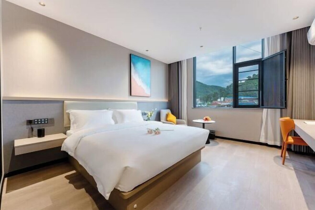 Une chambre d’hôtel moderne, dotée d’un grand lit, d’une table de chevet, d’une petite table avec une chaise et d’une fenêtre donnant sur l’extérieur.