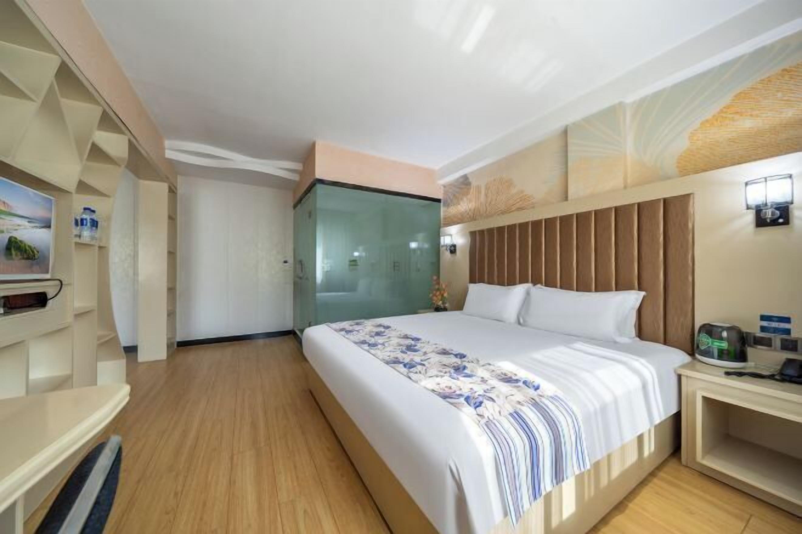 Une chambre d’hôtel avec un grand lit, une tête de lit en bois, une table de chevet avec une lampe et une cabine de douche en verre.