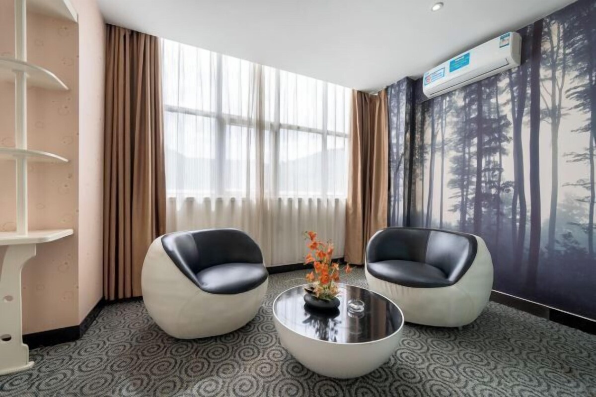 A modern room with two black leather chairs, a glass coffee table, and a large window with sheer curtains.