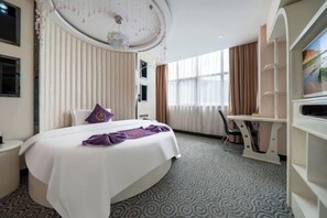 A hotel room with a bed, a desk, and a television on a stand.