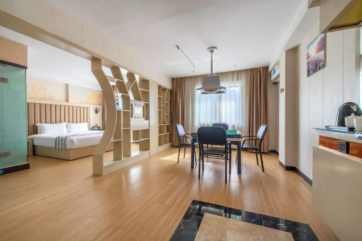 Een moderne hotelkamer met een houten vloer, een bed, een zithoek met stoelen, een tafel en een keukentoog.
