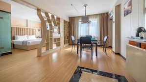 A modern hotel room with a wooden floor, a bed, a dining area with chairs, a table, and a kitchen counter.
