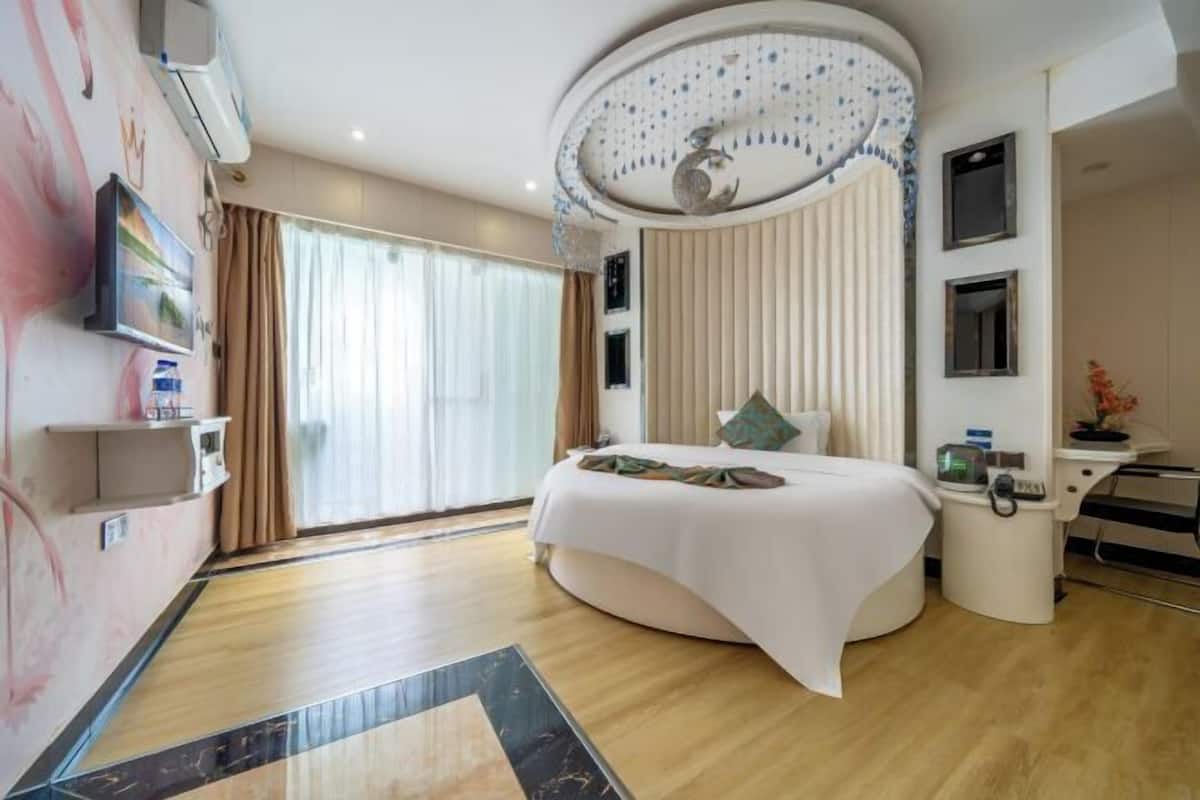 Een moderne hotelkamer met een gebogen bed, een groot raam met gordijnen, een plafond met decoratieve details en een klein bureau met stoel.
