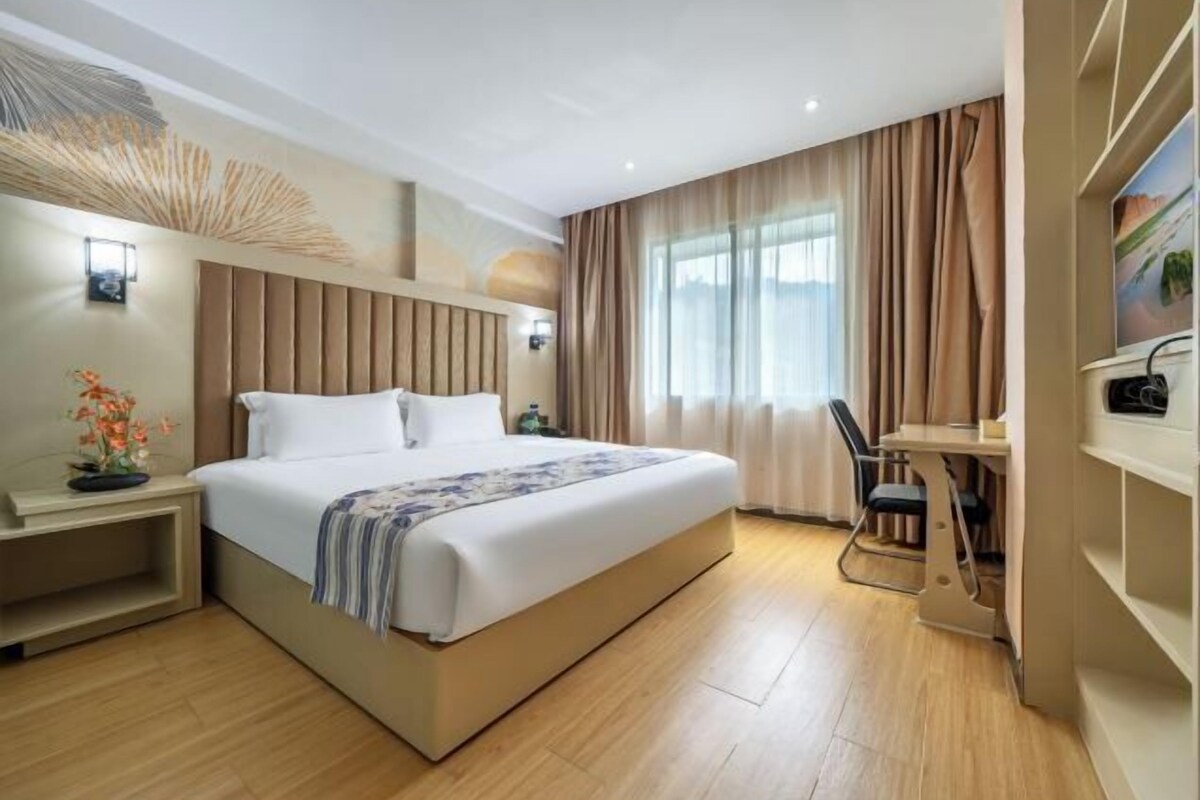 A modern hotel room with a large bed, bedside tables, a desk, and a window with curtains.
