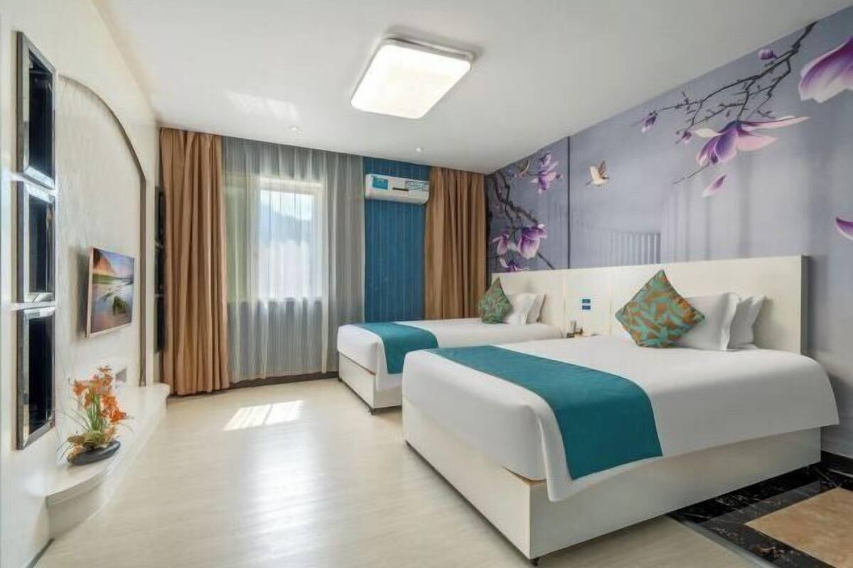 Een hotelkamer met twee bedden, een groot raam met gordijnen, een luchtverkoeler aan de muur en een bloemenmural.