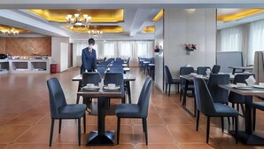 A hotel dining area with tables and chairs, a waiter, and a kitchen in the background. - Vienna Hotel (Hefei North 2nd Ring International Auto City) (Hefei)