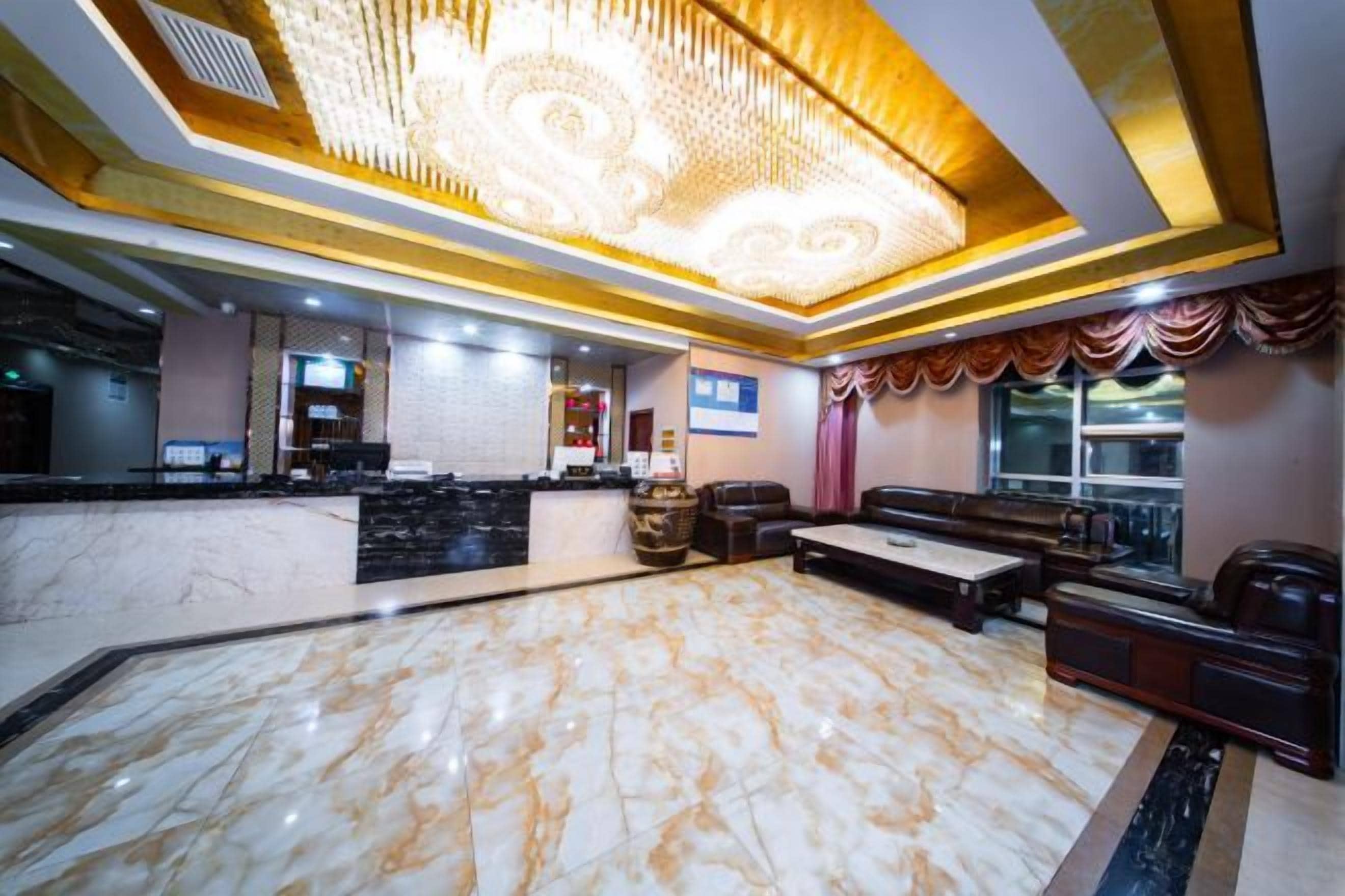 A hotel lobby with a marble reception desk, a seating area with sofas, and a large chandelier.