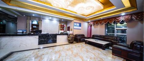 A hotel lobby with a marble reception desk, a seating area with sofas, and a large chandelier.