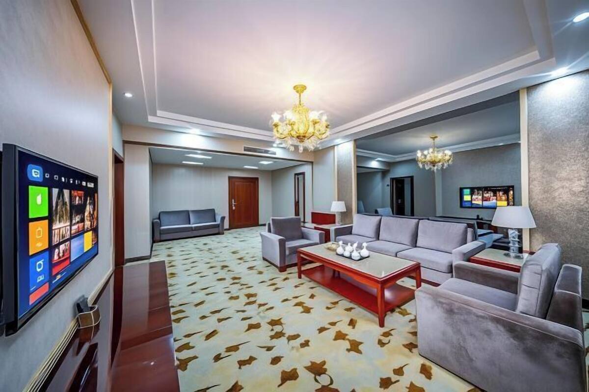 A hotel room with a large flat-screen TV, a sofa set, a coffee table, and a chandelier.