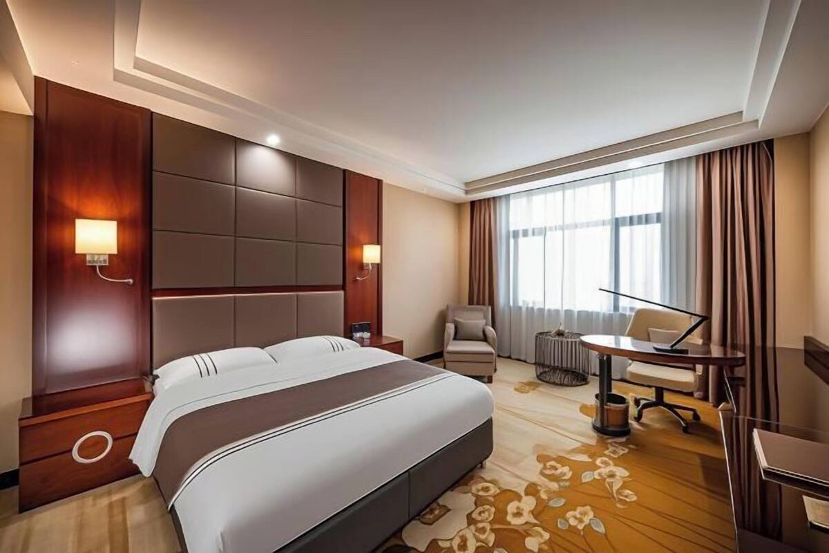 A hotel room with a large bed, a desk, a chair, and a sofa.