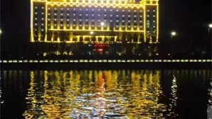A large hotel with a symmetrical facade, multiple floors, and a reflection in the water below.