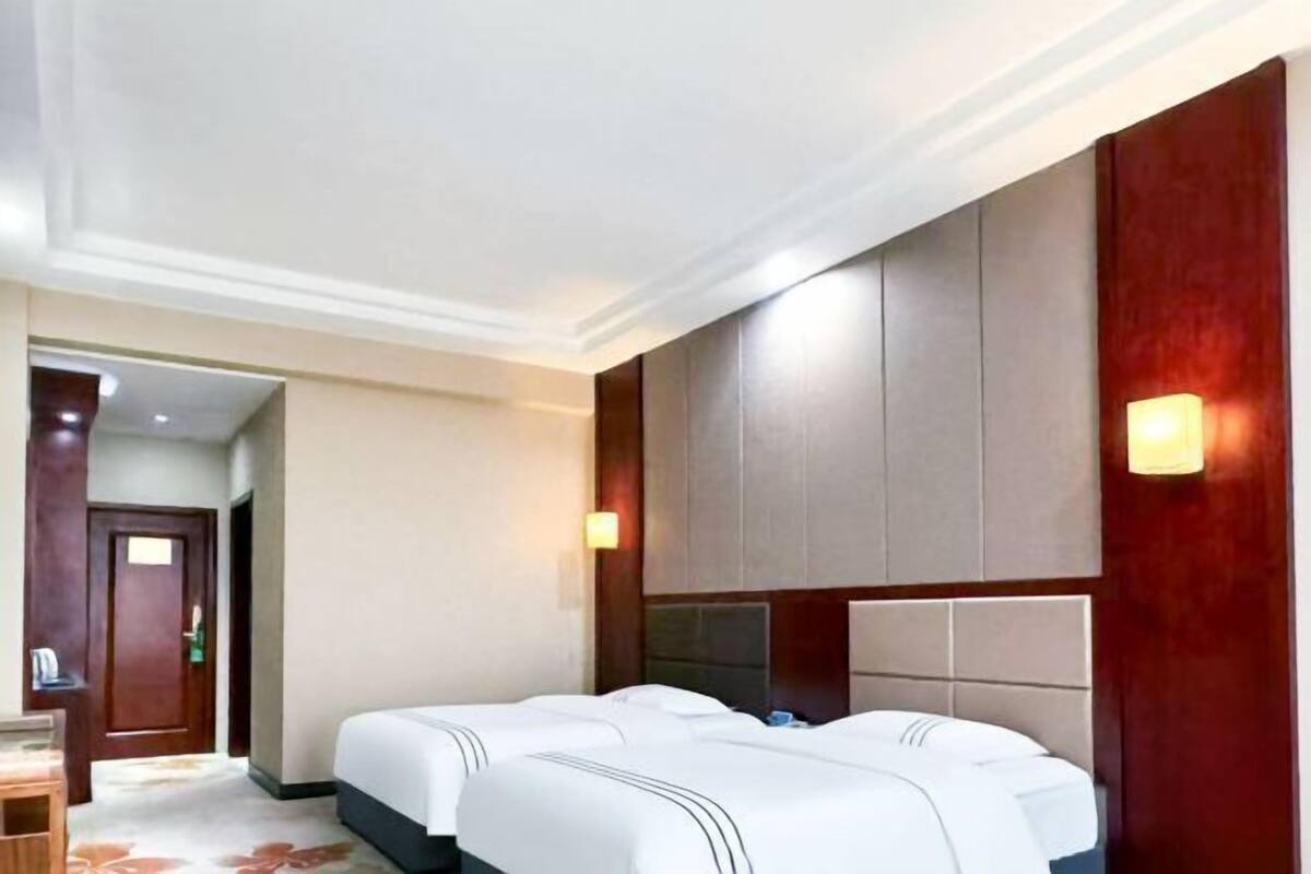 A hotel room with two beds, a wooden door, a desk, and a nightstand.