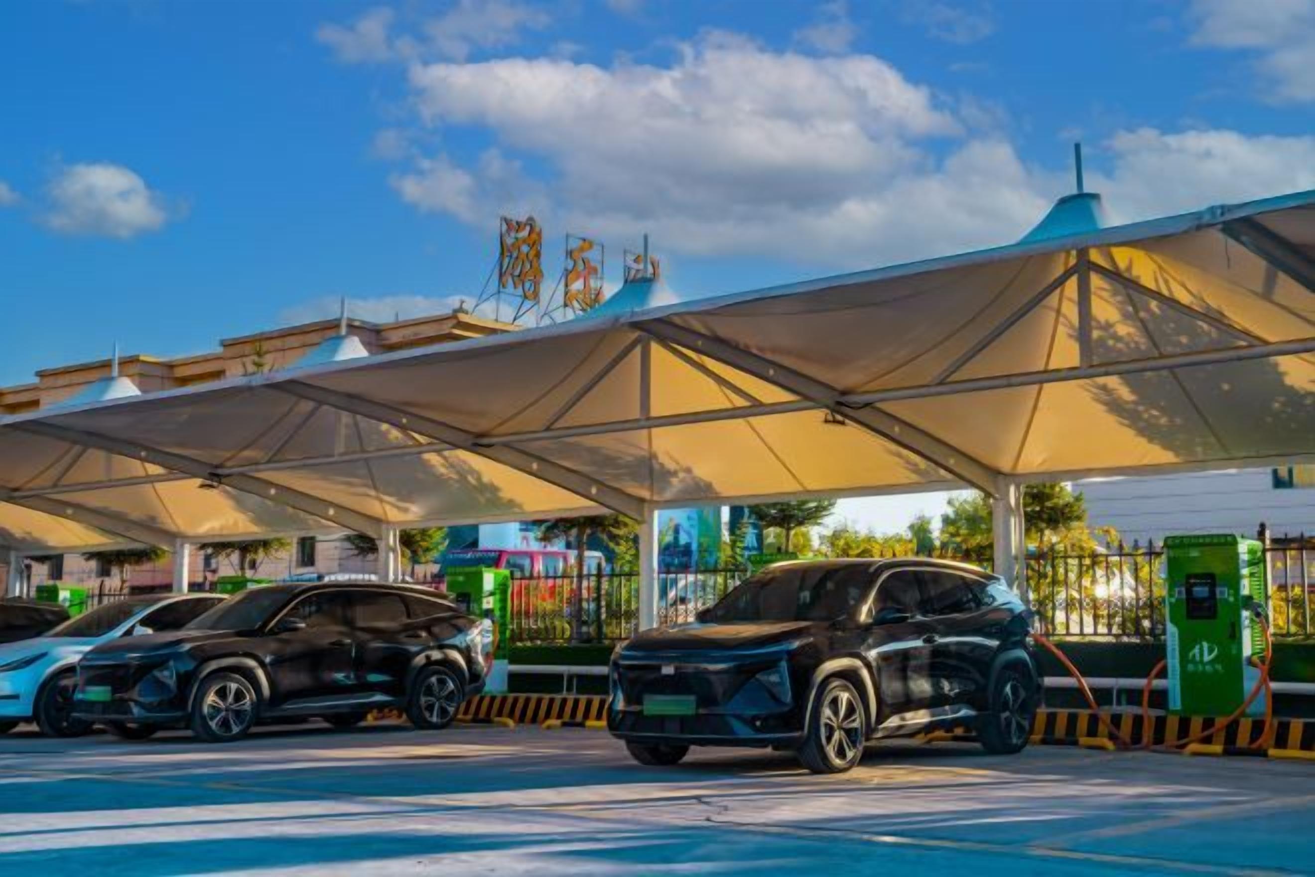 Un área de estacionamiento techada con varios vehículos, una estructura tipo marquesina y una estación de carga para vehículos eléctricos verdes.