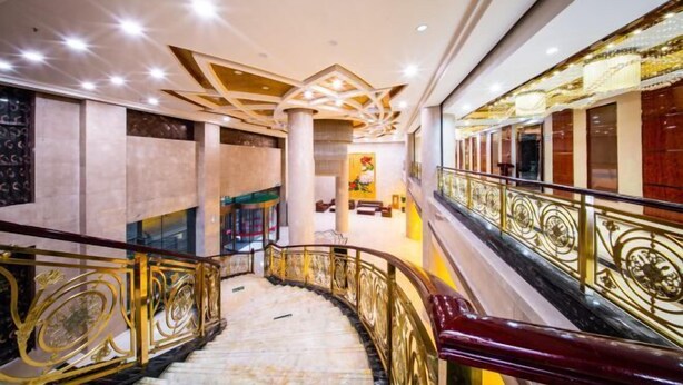 A grand interior with a marble staircase, ornate railings, and a high ceiling with geometric patterns.