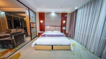 Habitación de hotel con una cama grande, zona de estar con sillas, tocador con espejo y un ventanal con cortinas.