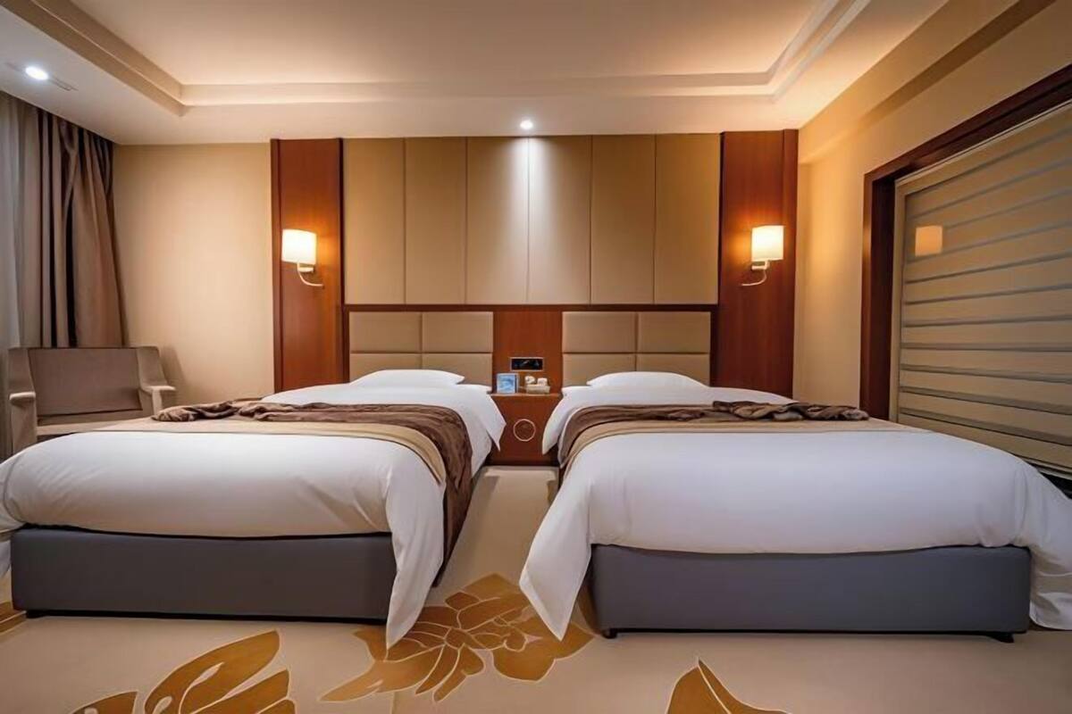 A hotel room with two beds, a headboard with built-in lighting, a bedside table, and a chair.