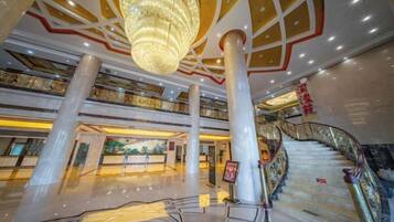 A spacious lobby with a grand chandelier, multiple floors, and a staircase.