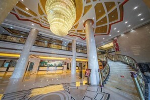 Eine geräumige Lobby mit einem prunkvollen Kronleuchter, mehreren Etagen und einer Treppe.