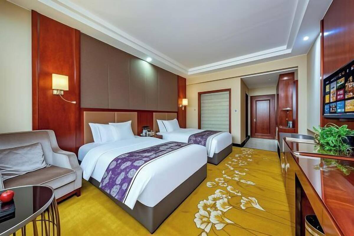 A hotel room with two beds, a sofa, a small table, and a TV.