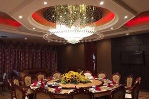 Une salle à manger élégante, avec une grande table ronde, des chaises richement décorées, un lustre et un téléviseur fixé au mur.