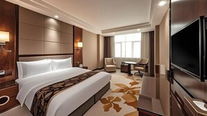A hotel room with a large bed, a flat-screen TV, a desk with a chair, and a window with curtains.