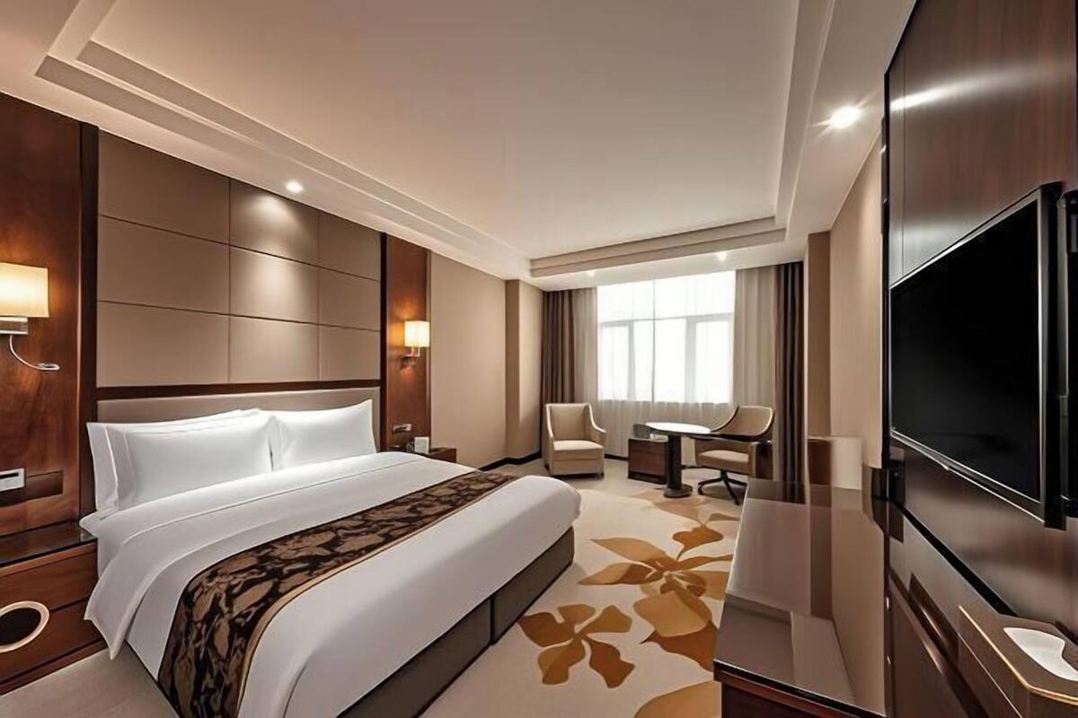 A hotel room with a large bed, a flat-screen TV, a desk with a chair, and a window with curtains.