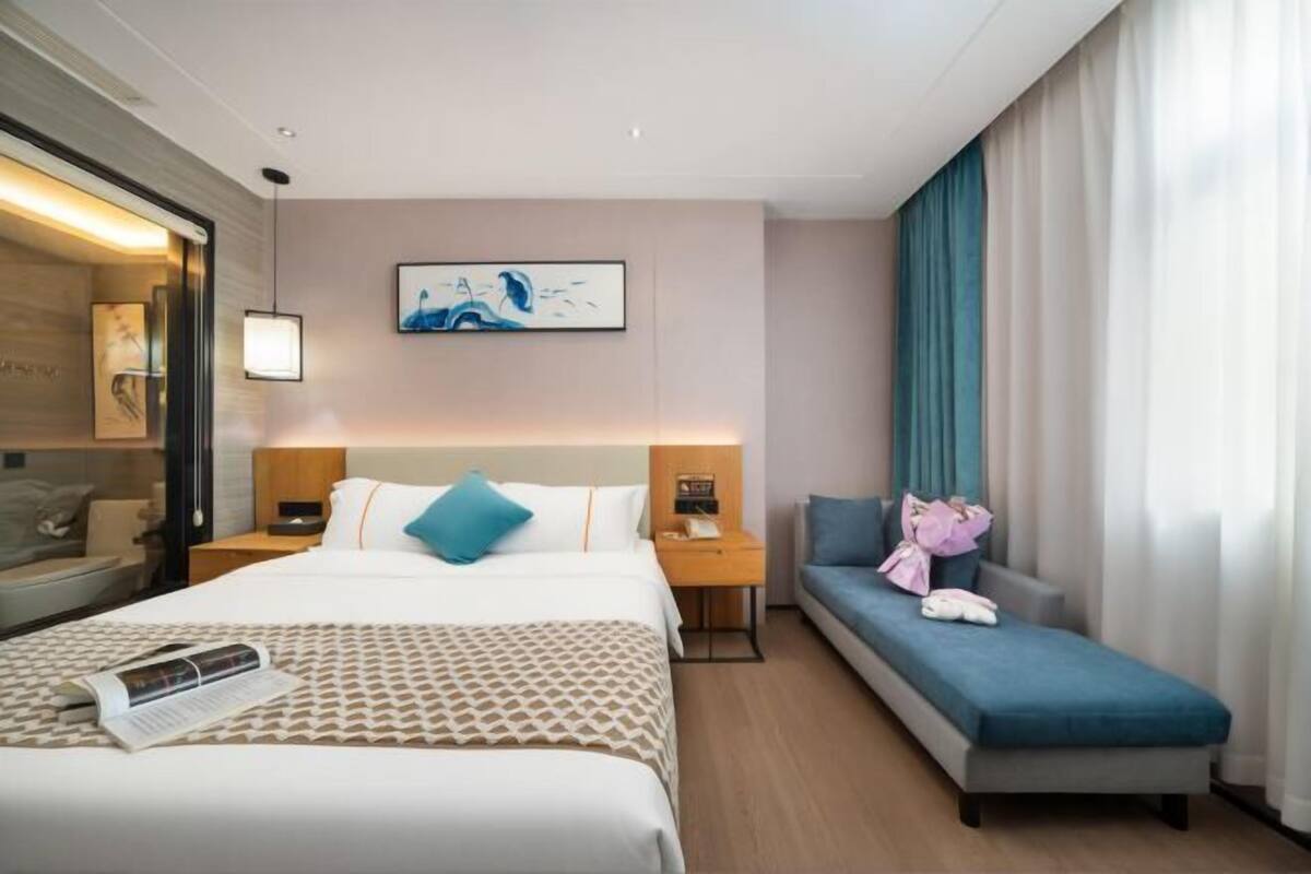 A hotel room with a bed, a bedside table with a lamp, a sofa, and a wall-mounted artwork.