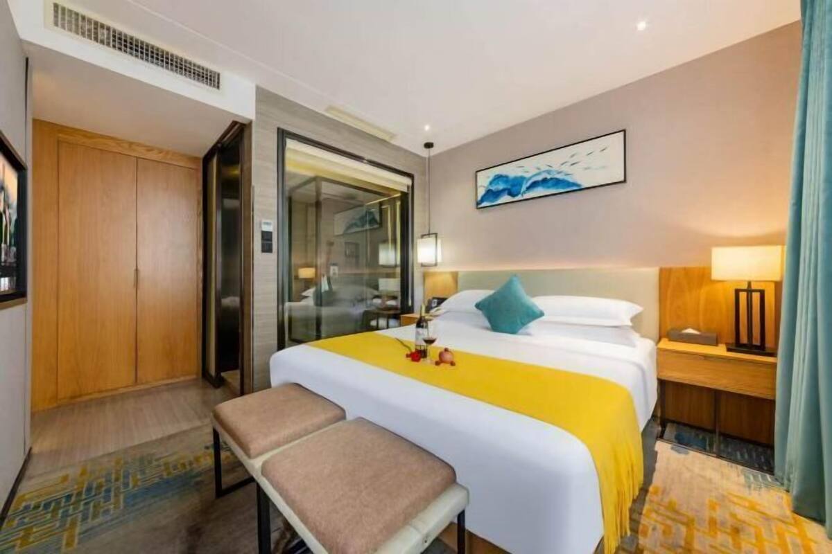 A hotel room with a bed, a bench, a bedside table, a lamp, and a painting on the wall.