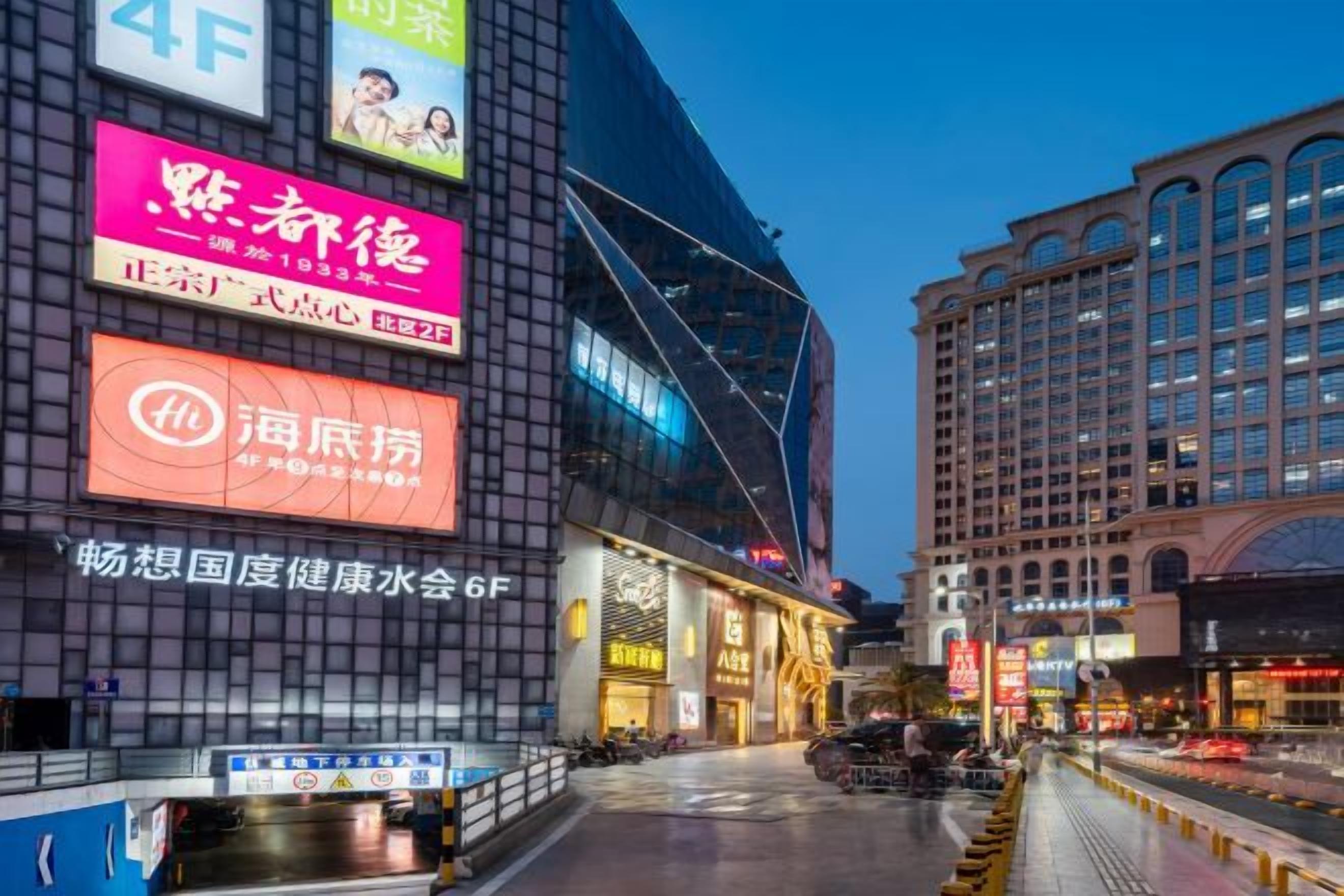 A multi-story building with illuminated signage, a pedestrian walkway, and a street view.
