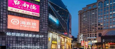 A multi-story building with illuminated signage, a pedestrian walkway, and a street view.