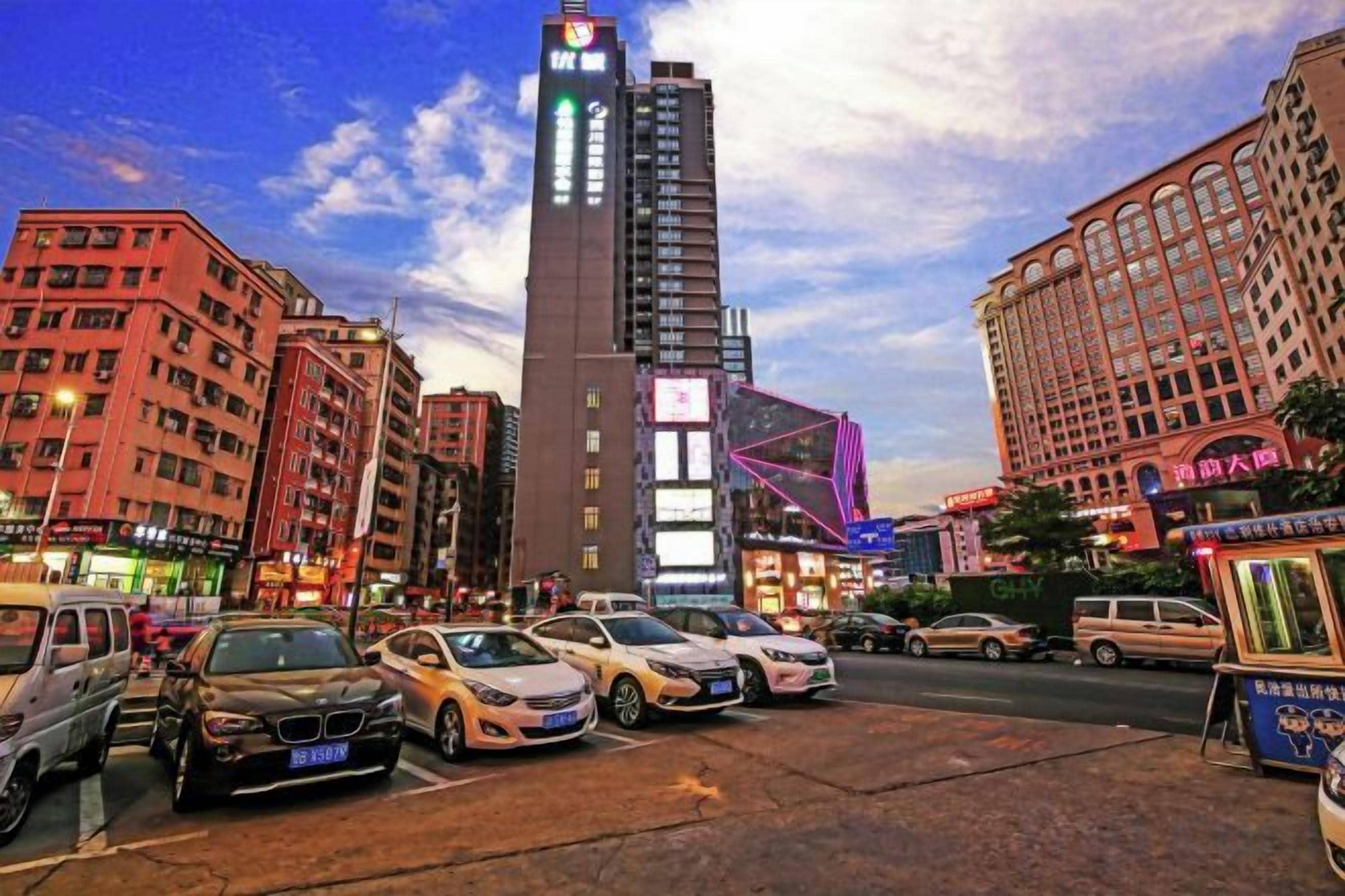 Une vue urbaine avec des bâtiments modernes, une tour imposante et un parking rempli de voitures.