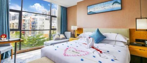 Habitación de hotel con un ventanal grande, una cama con decoración en forma de corazón, un escritorio y una silla.