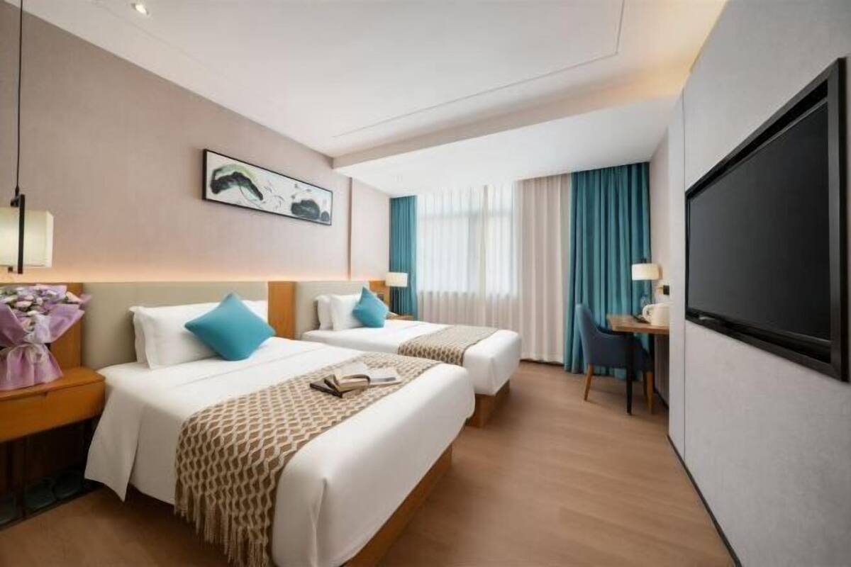 A hotel room with two beds, a desk, a chair, a TV, and a window with curtains.