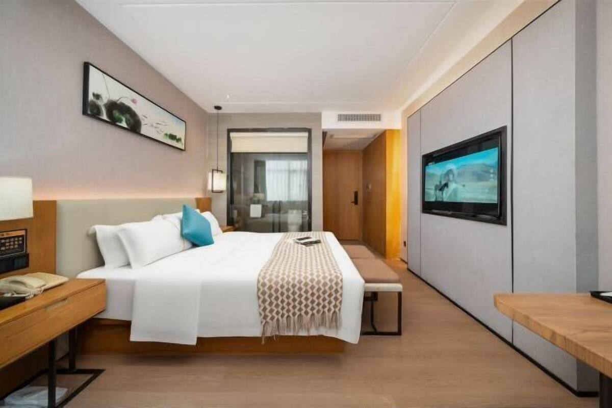 A modern hotel room with a bed, bedside table, bench, TV, and artwork on the walls.