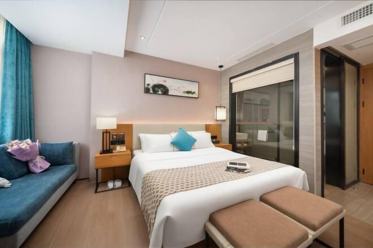 A hotel room with a bed, a sofa, a desk, and a large window.