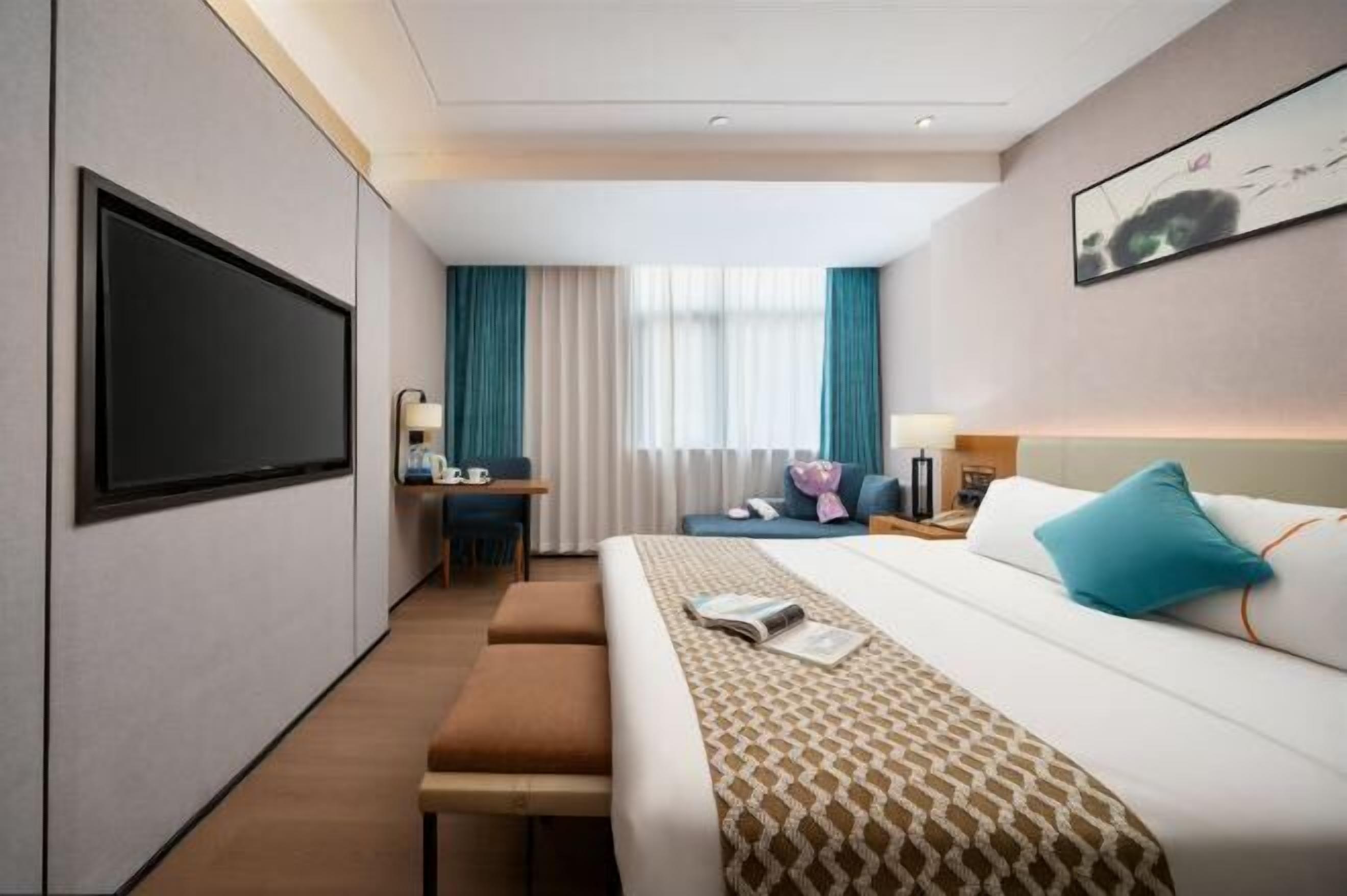 A hotel room with a large bed, a desk, a chair, a TV, and a window with curtains.