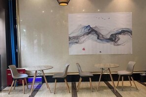 Un interior moderno con una mesa redonda y cuatro sillas, un cuadro abstracto grande en la pared, y un objeto rojo a la izquierda.